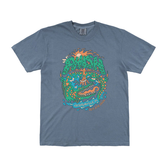 A slate blue crewneck t-shirt featuring a colorful graphic print of a stylized alligator surrounding trees and water, with the text 'Phish' and 'Jacksonville, FL, Oct. 9th, 2026' on a white background.